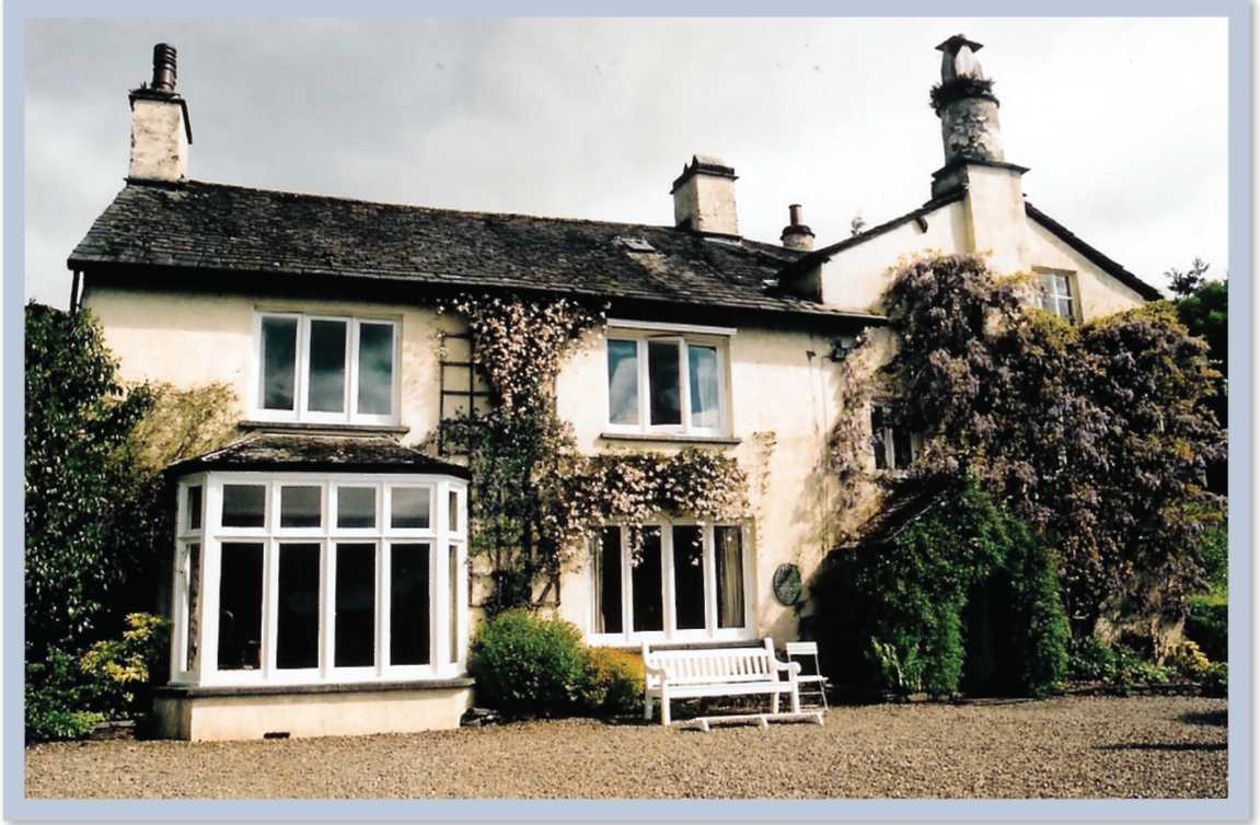 A large home with several windows and overgrown shrubs and trees against the home.