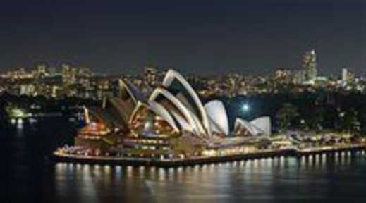 The Sydney Opera House at night. Water surrounds the house and city lights are behind it.
