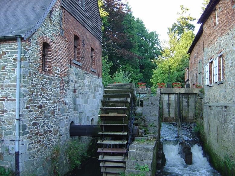 photo of a water wheel connected to the side of building with canal water rushing to the side