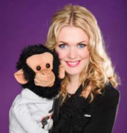 A woman smiles next to a monkey puppet.