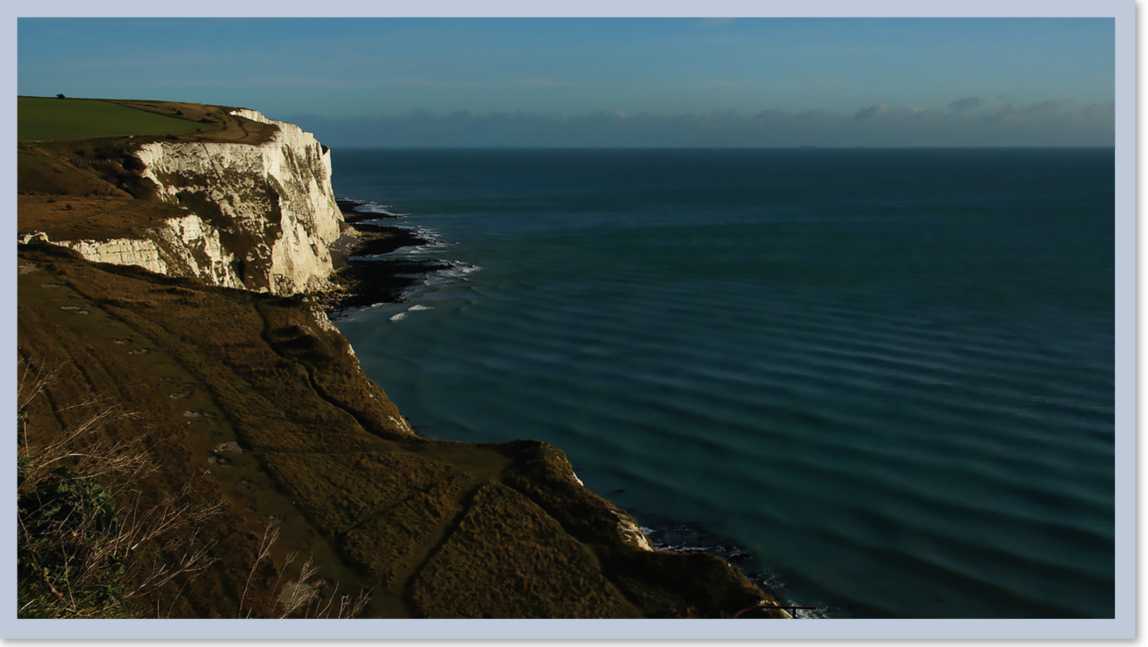 A grassy land on a cliff which overlooks a body of water.