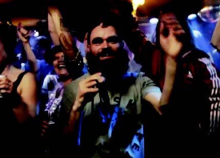 A person wearing sunglasses and holding the hands up in front of a crowd Description automatically generated with low confidence