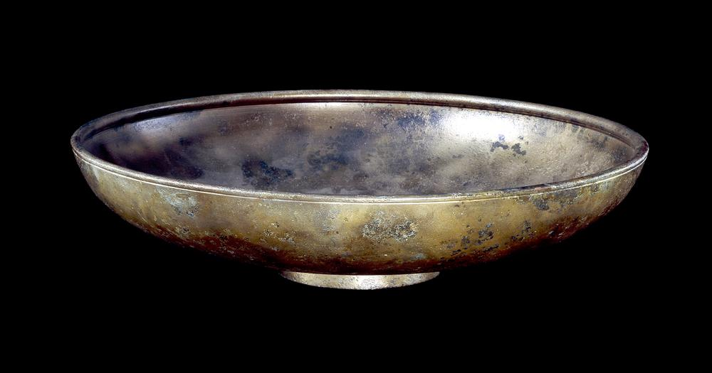 A shallow bowl made of copper and showing weathering from age.