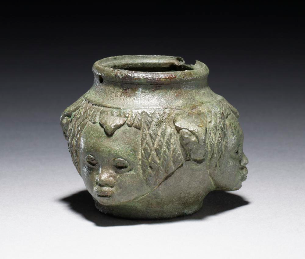 An oil flask, apparently missing its lid, decorated with an African face on each of the four sides of the round jar.