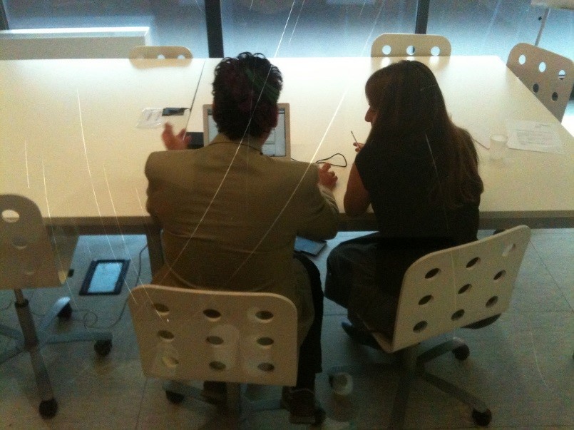 A photograph of a usability test without a lab. Two people are sitting at a table with a tablet, actively conversing.